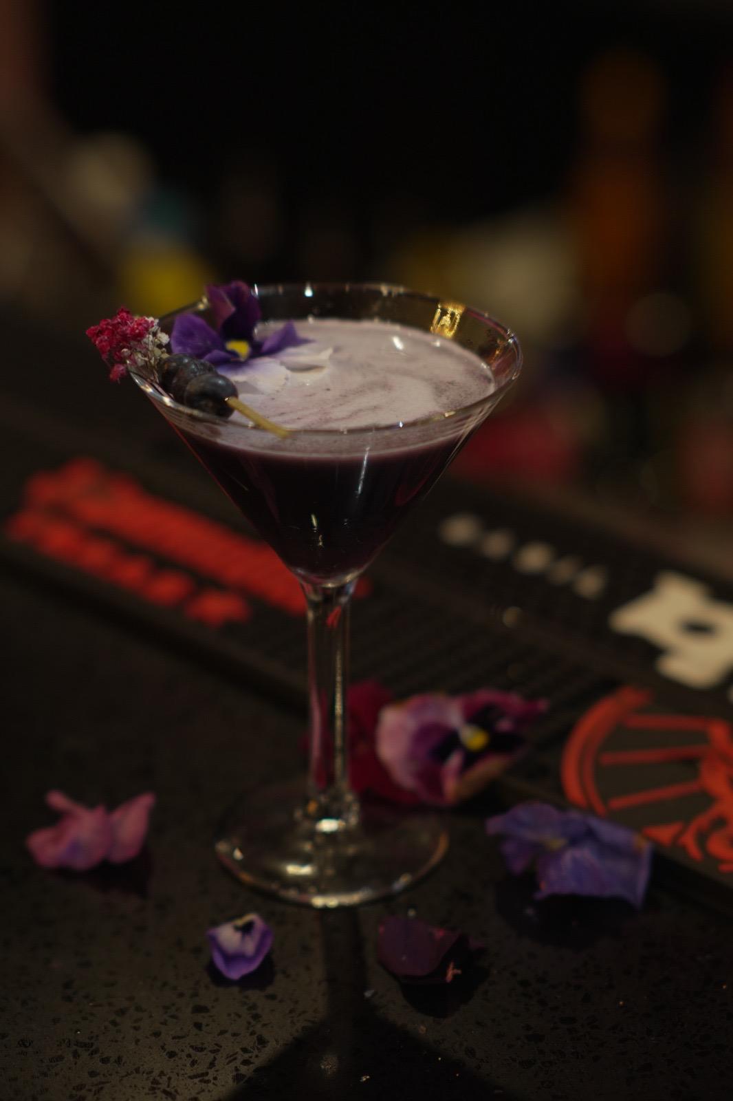 Berry Bliss purple cocktail in a martini glass with edible flower garnish