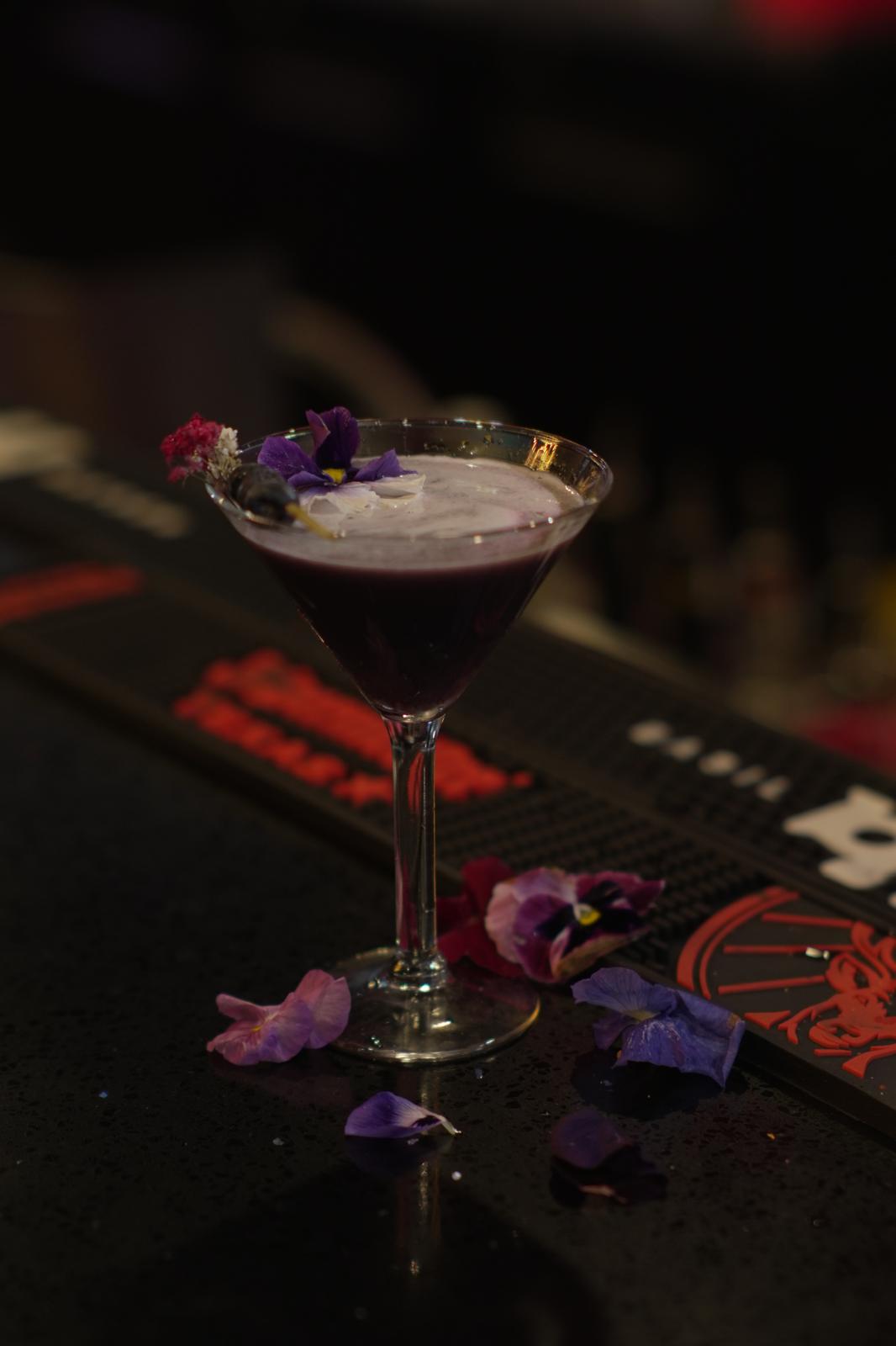 Berry Bliss cocktail with floral garnish on a dark bar
