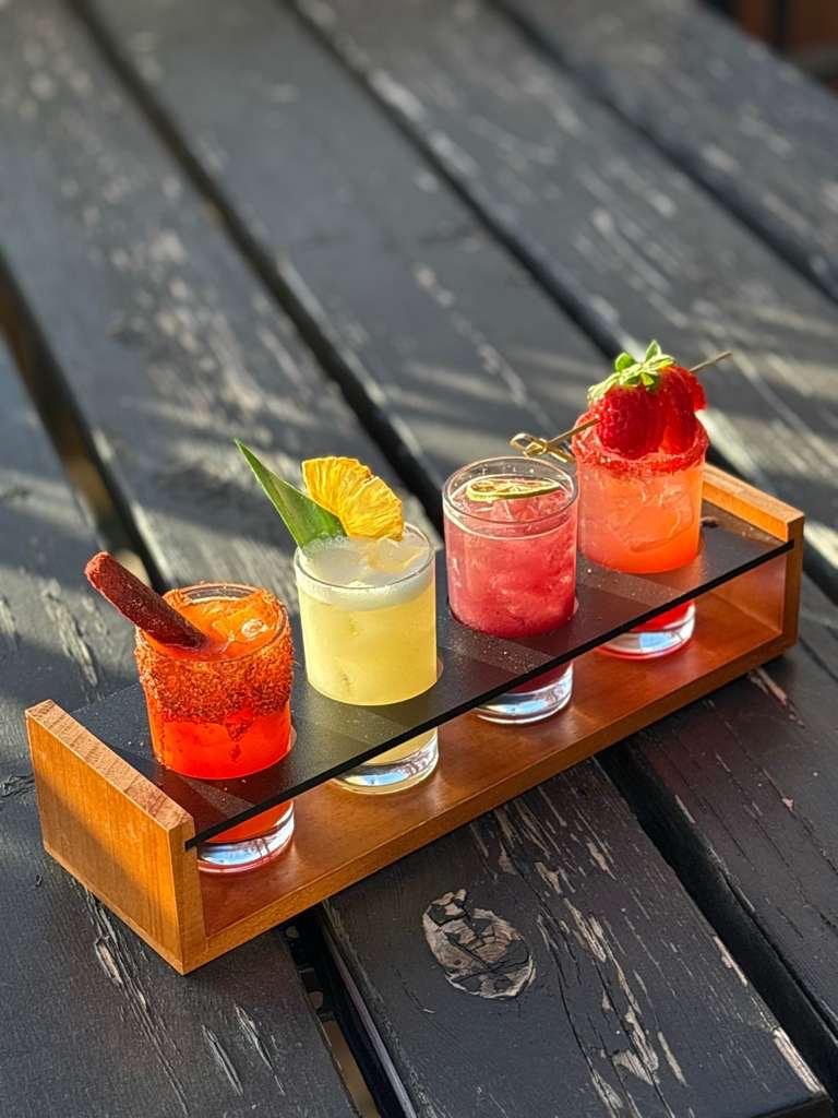 Colorful cocktail flight with four drinks on a wooden paddle